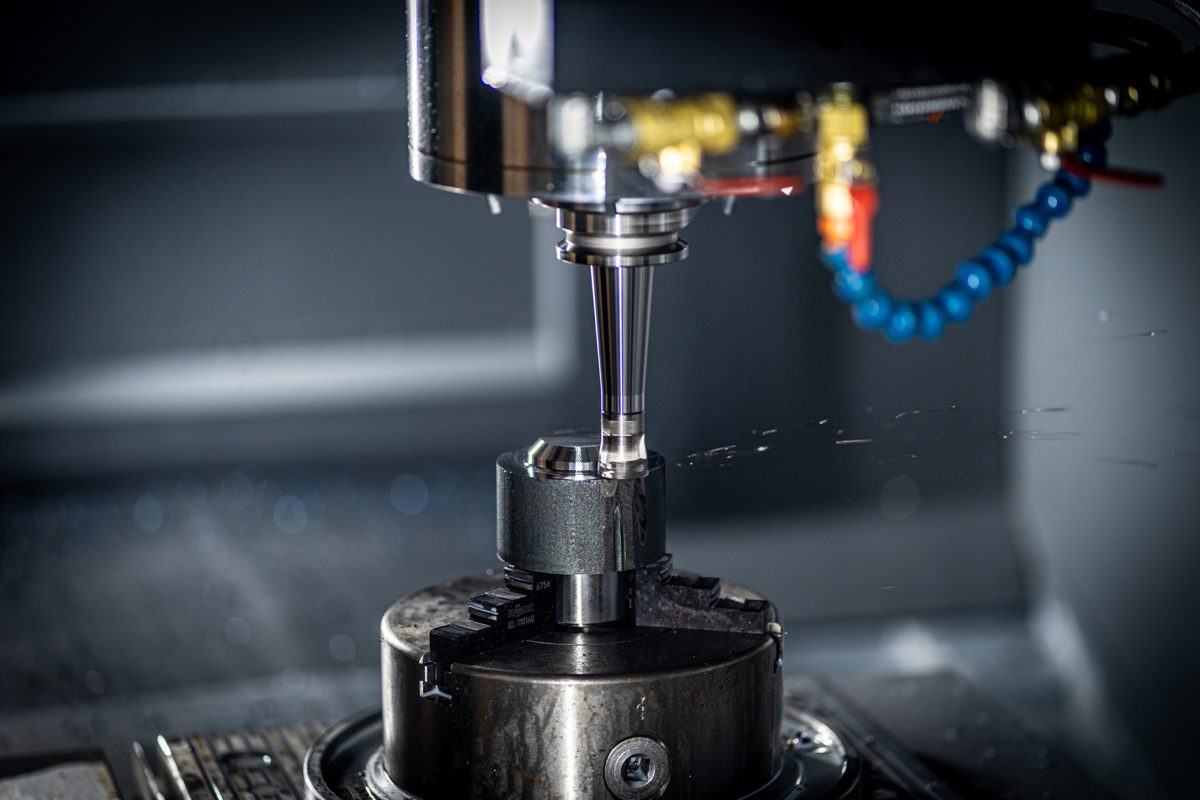 A CNC spindle close-up in industrial blue light — the system, the machinery, the precision tool meeting material