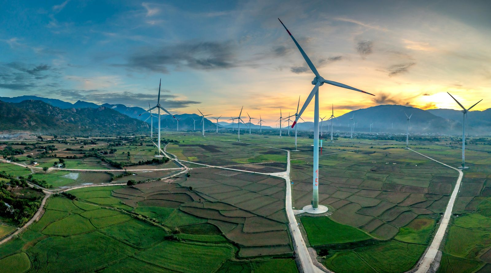 Aerial view of wind turbines across a rural agricultural landscape at golden hour with mountain backdrop