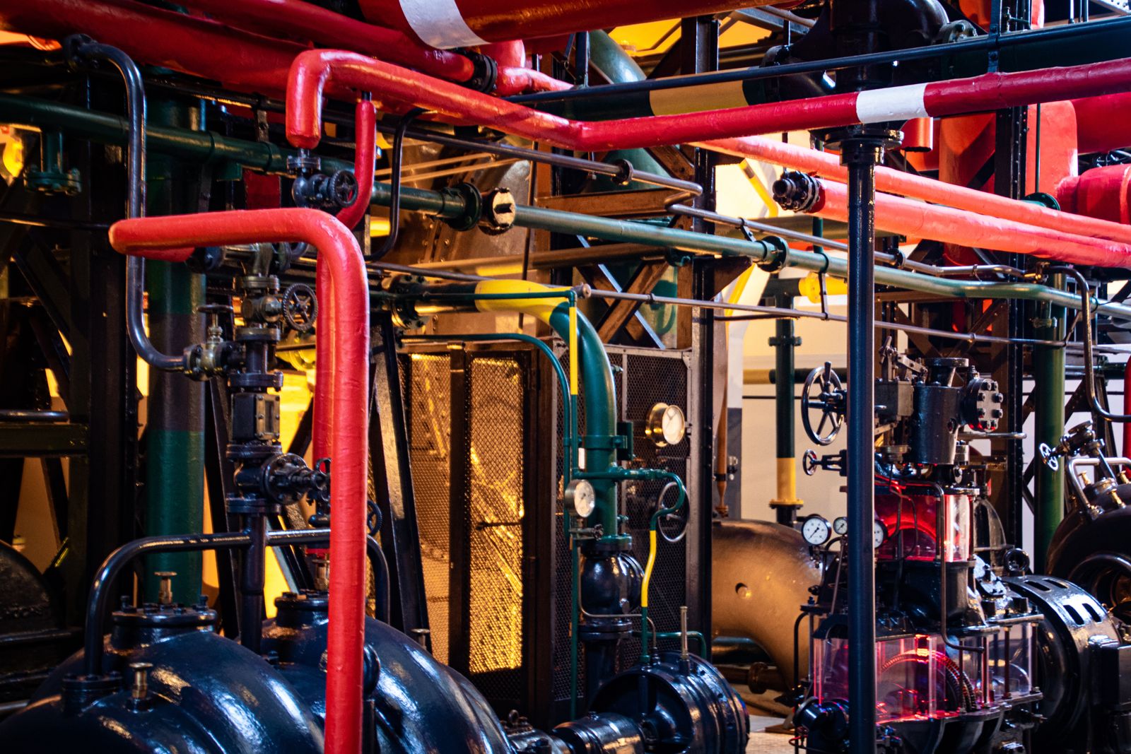 Densely-packed Victorian-era industrial pipework in red, green and brass — the factory floor the consulting industry was founded inside before it forgot.