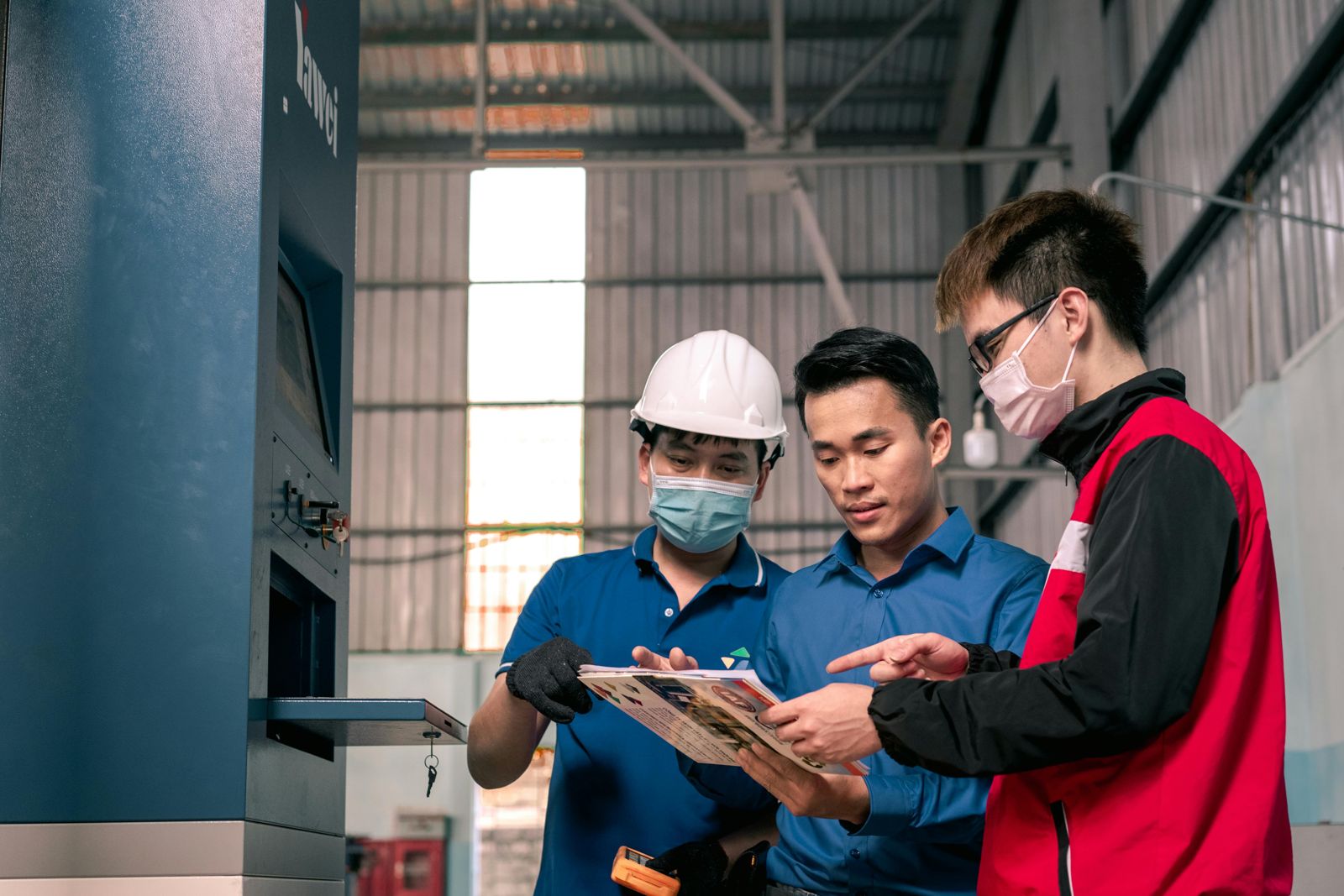 Three workers in full PPE gathered around a tablet inside a contained production space — the moment the strategy deck meets the factory floor.