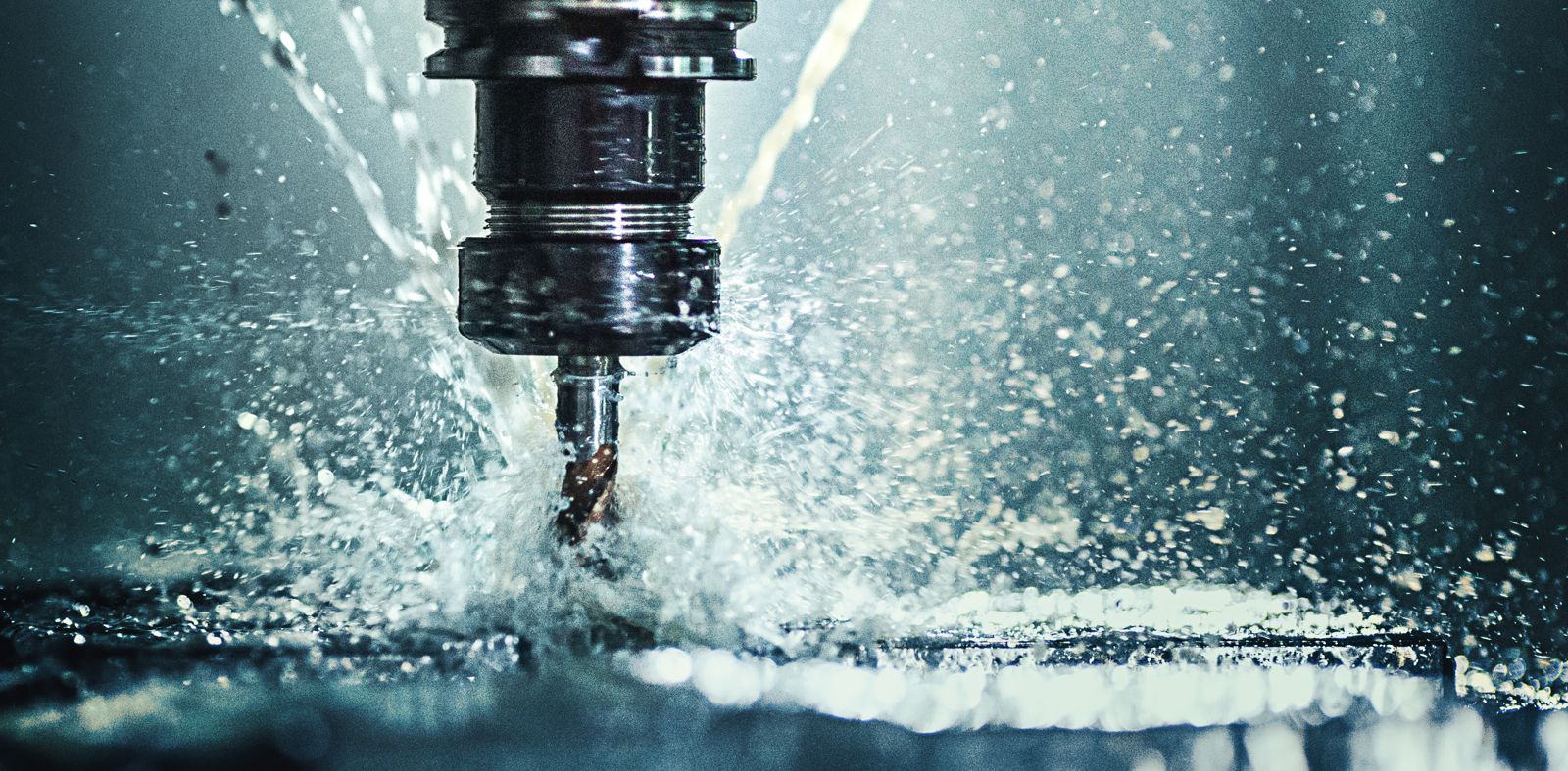 CNC drill bit cutting metal with a dramatic coolant spray, water droplets frozen mid-flight, blue-green light