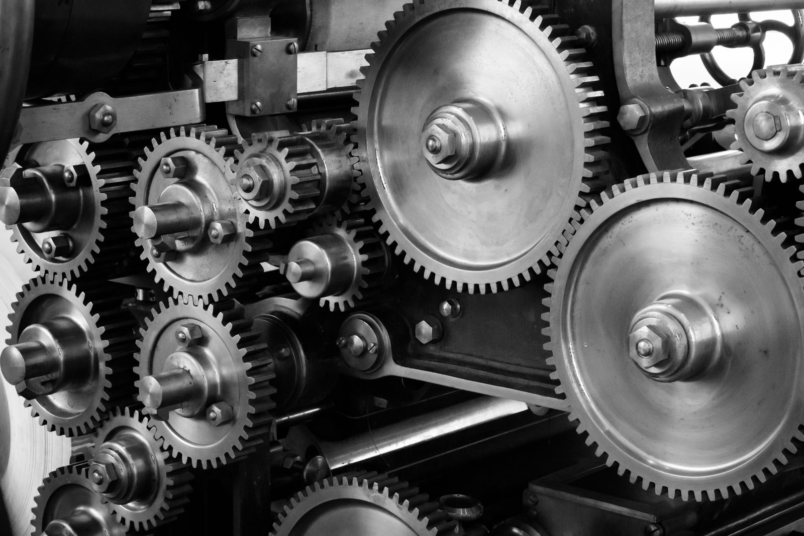 Black-and-white close-up of a large mechanical gear train, interlocking cogs meshed under load