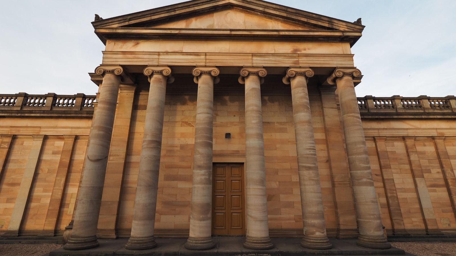Neoclassical sandstone facade with six Ionic columns under a plain pediment, warm low light