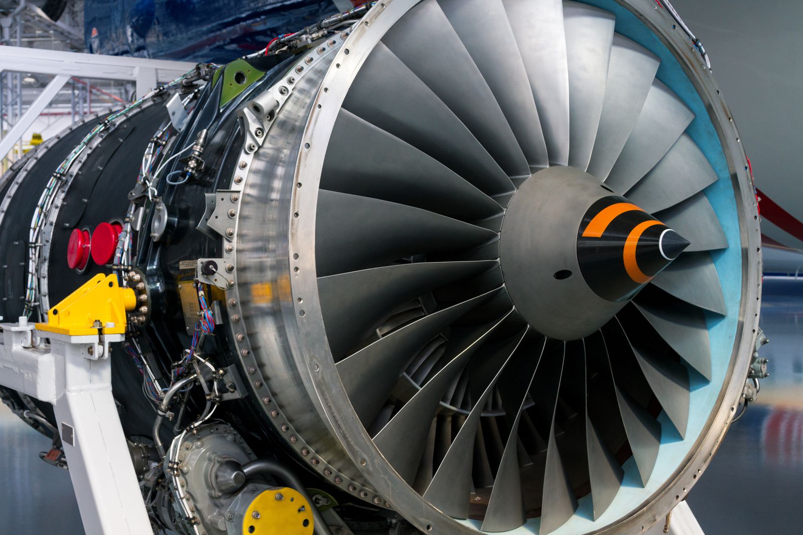 Close-up of a jet-engine turbofan in an aerospace hangar, gleaming turbine blades and orange-striped nose cone — thousands of parts from every discipline integrated into one system that must hold together while it runs