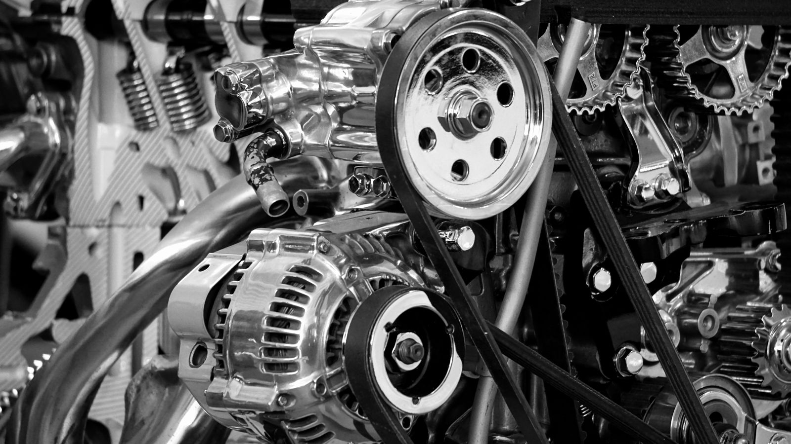 Black-and-white close-up of an engine bay, belts running over pulleys past an alternator and cam gears
