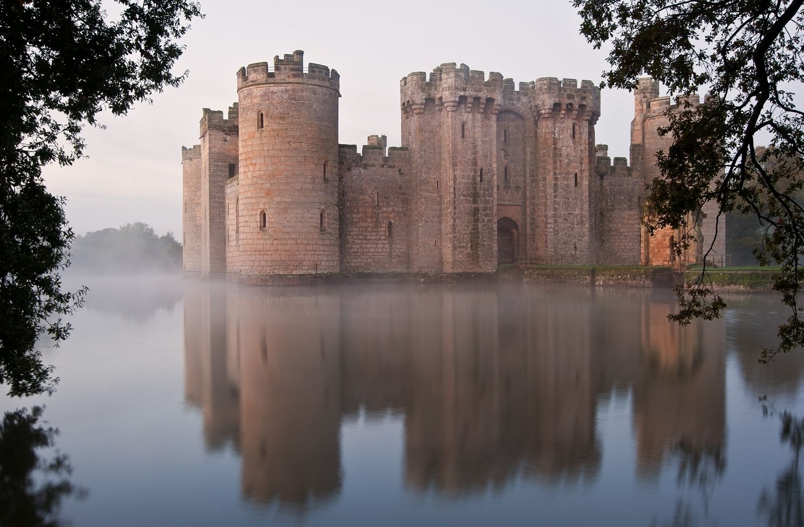 Bodiam Castle rising from a still misty moat at dawn, English medieval fortress reflected in the water