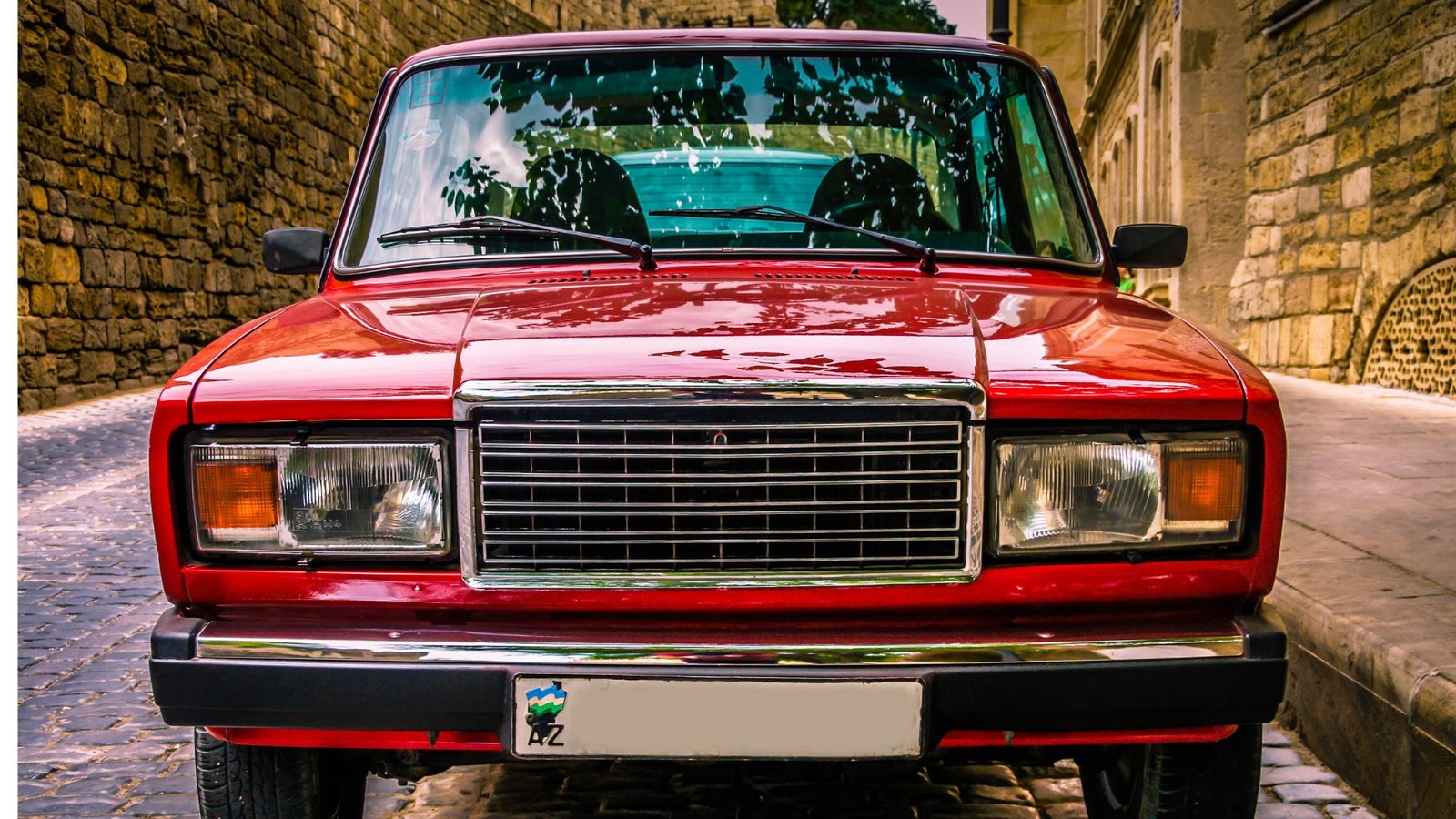 Red Lada head-on in a cobbled street, chrome grille and round headlamps, a design tooled once and produced for decades