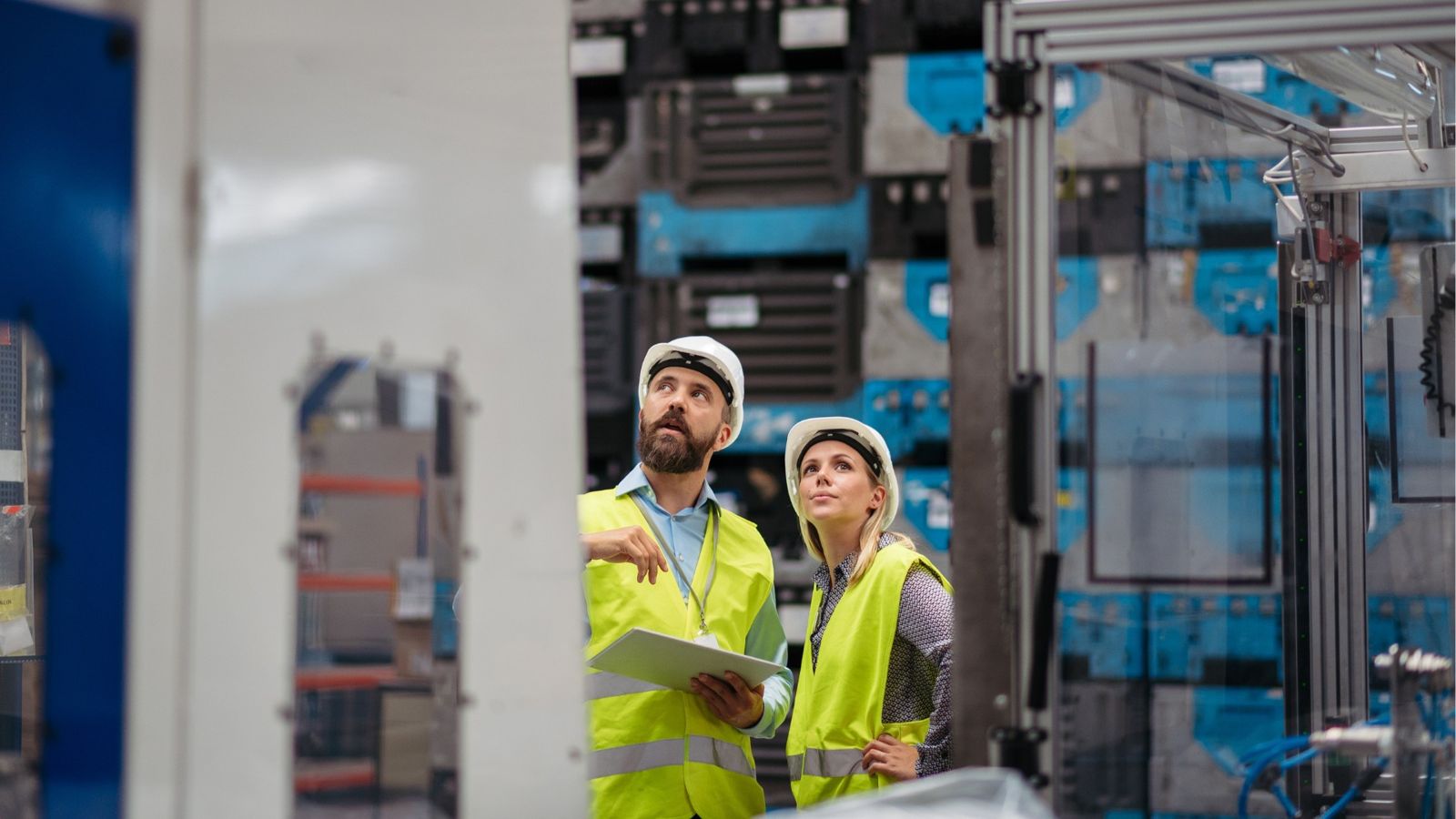 Two engineers in white hard hats and yellow hi-vis vests looking up at machinery, one holding a tablet — modern industrial commissioning