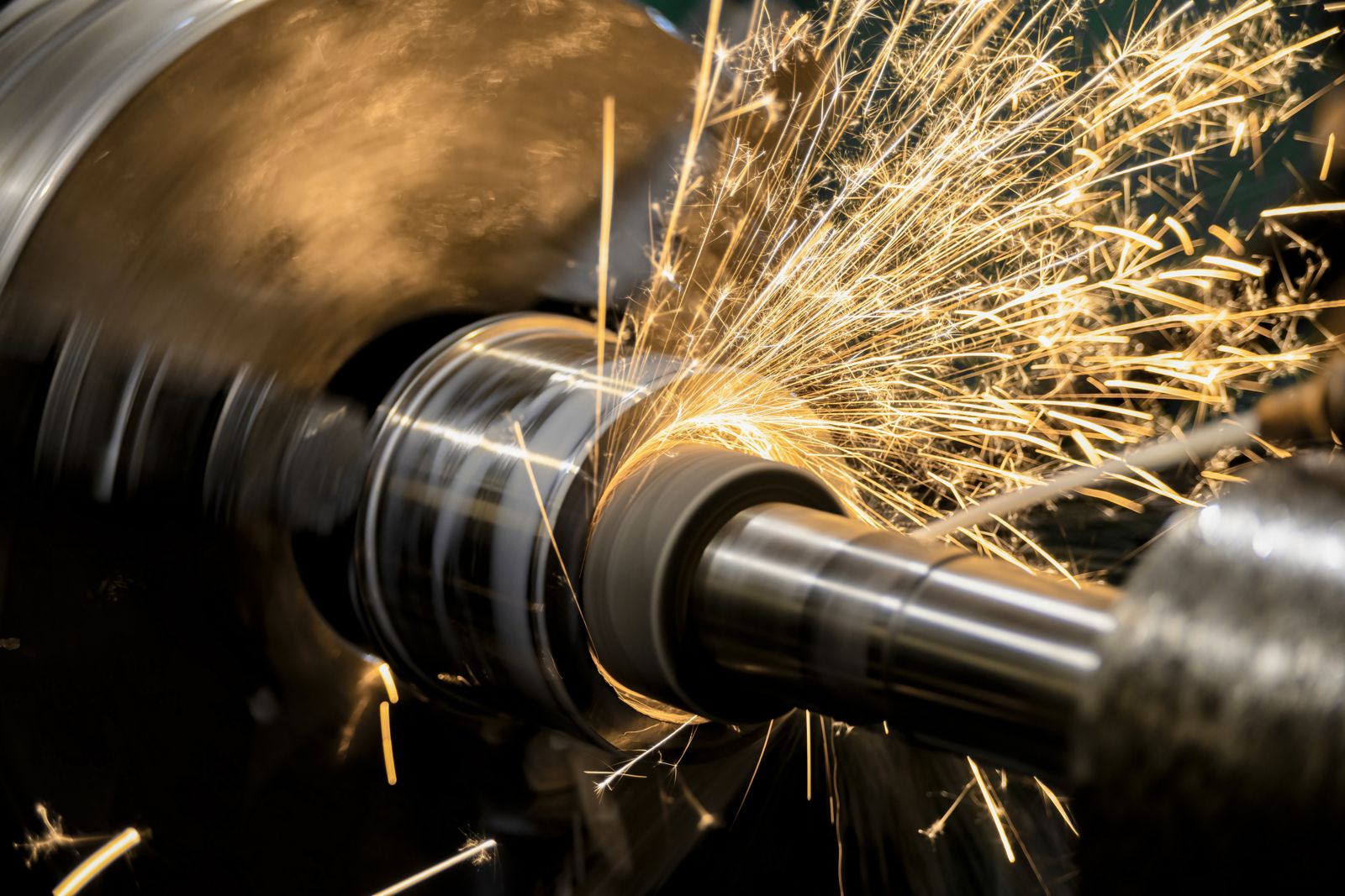 Lathe operation throwing golden spark trails during grinding, dark workshop frame