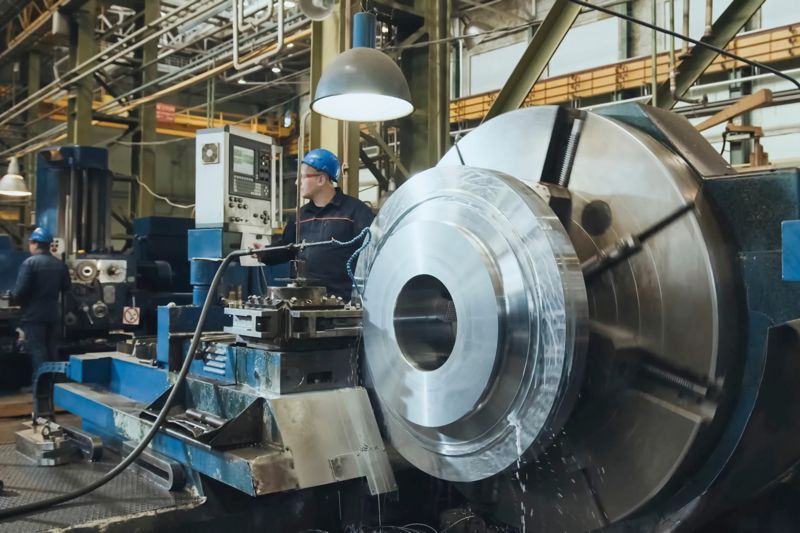 A machinist at the panel of a large horizontal lathe, coolant running
